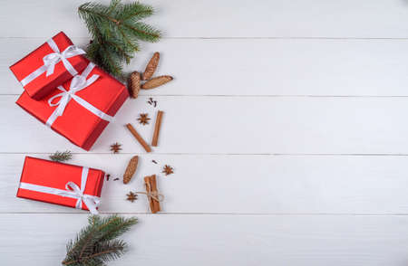 Christmas background with red gift boxes, fir branches, pine cones, cinnamon sticks and stars anise, free space. Red Christmas gift boxes on white wooden background, copy space. Flat lay, top viewの写真素材