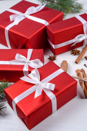 Christmas background with red gift boxes, fir tree branches, pine cones, cinnamon sticks and stars anise. Red Christmas gift boxes on white wooden background. Holiday greeting cardの写真素材