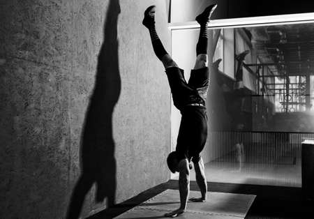 Athlete doing push ups on his hands while standing upside down near red wall. Workout lifestyle...