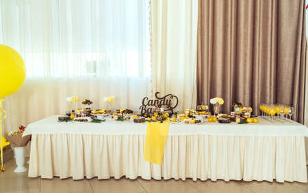 Holiday candy bar in yellow and brown color. Wedding candy bar served with cupcakes, cake pops, desserts in glasses, lemons and coffee beans の写真素材