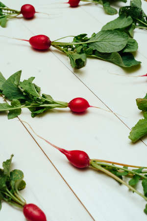 Fresh organic red radishes with tops and green leaves on white wooden background. Top view. Vegetable backgroundの写真素材