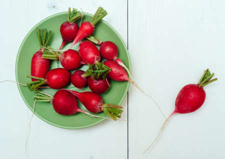 Fresh organic red radishes on green plate on white wooden background. Top view. Vegetable background. Free space for textの写真素材