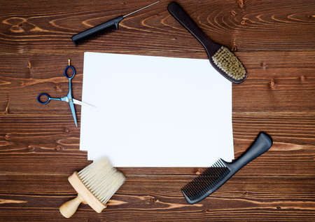 Hairdresser tools on wooden background. Blank card with barber tools flat lay. Top view on wooden table with scissors, comb and brush with empty white paper, free spaceの写真素材