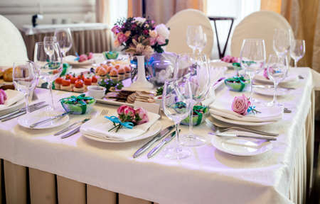 Pink roses with blue ribbon on white empty plate with white napkin on dinner table in blur. Table setting. Table served for wedding banquet, close up viewの写真素材