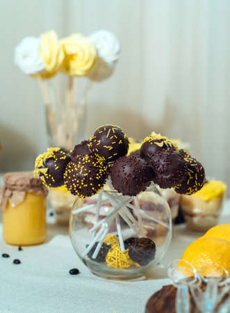 Chocolate cake pops in glass vase on wedding candy bar. Holiday candy bar in yellow and brown colorの写真素材