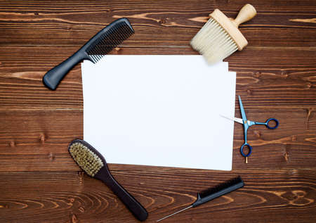 Hairdresser tools on wooden background. Blank card with barber tools flat lay. Top view on wooden table with scissors, comb and brush with empty white paper, free spaceの写真素材