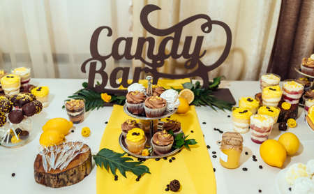 Holiday candy bar in yellow and brown color. Wedding candy bar served with cupcakes, cake pops, desserts in glasses, lemons and coffee beans の写真素材