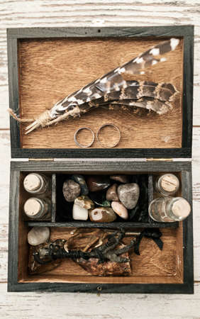 Wooden box with wedding rings, bird's paws, feathers, empty bottles and stones on wooden background. Wedding decorationsの写真素材