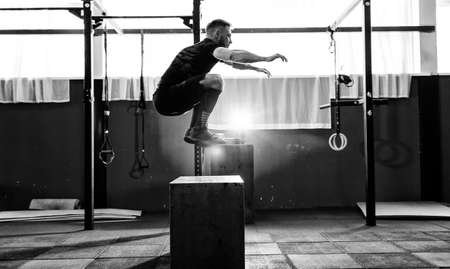 Fit young man jumping onto a box as part of exercise routine. Man doing box jump in the gym. Athlete is performing box jumps の写真素材