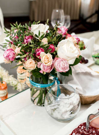 Beautiful wedding bouquet of cream and pink roses in glass vase on dinner table, selective focus. Table setting at a luxury wedding reception. Flowers on the tableの写真素材