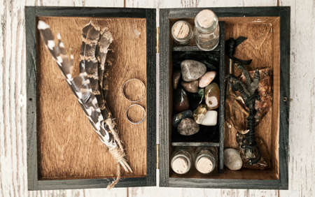 Wooden box with wedding rings, bird's paws, feathers, empty bottles and stones on wooden background, free space. Wedding decorationsの写真素材