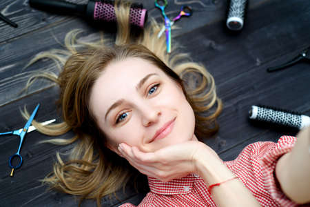 Selfie photo of  happy smiling young woman in plaid shirt with hairdresser tools among her の写真素材
