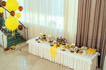 Holiday candy bar in yellow and brown color. Wedding candy bar served with cupcakes, cake pops, desserts in glasses, lemons and coffee beans の写真素材