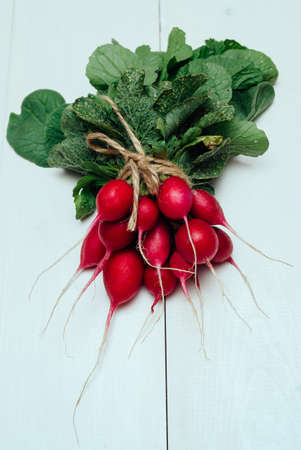 Bunch of fresh organic red radishe with tops and green leaves on white wooden background. Vegetable...