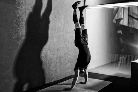 Athlete doing push ups on his hands while standing upside down near red wall. Crossfit training. Workout lifestyle concept.  Full body length portraitの写真素材