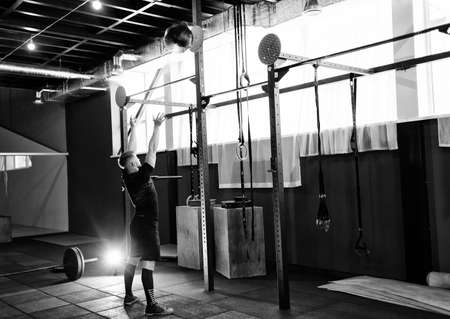 Muscular man doing exercise with medicine ball in gym.  Young man doing upper body exercise working out with heavy weighted ballの写真素材