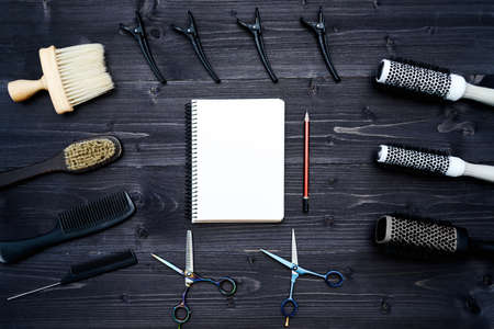 Hairdresser tools on wooden background. Blank card with barber tools flat lay. Top view on wooden table with scissors, comb, hairbrushes and hairclips with empty notebook and pencil, copy spaceの写真素材