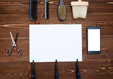 Hairdresser tools on wooden background. Blank card with barber tools flat lay. Top view on wooden table with scissors, comb and brush with empty white paper and phone, copy spaceの写真素材