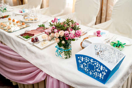 Beautiful wedding bouquet of cream and pink roses in glass vase on dinner table next to blue box for money, selective focus. Flowers on the tableの写真素材
