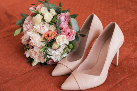 Beautiful lush wedding bouquet of white and pink peony and roses near bride's shoes on bedの写真素材