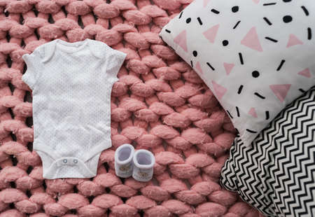 Baby clothes and shoes for newborn in pastel colors on pink merino wool blanket. Set of baby clothes. Body and booties for newborn on the bed. Pink merino wool blanketの写真素材