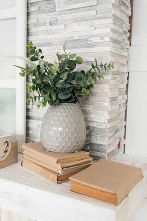 Gray vase with eucalyptus on pile of books near stone wall. Eucalyptus branches in vaseの写真素材