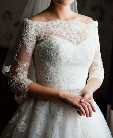 Beautiful young bride in white dress waiting for the groom indoors. Elegant charming young brunette bride posing indoors in wedding dress. Morning, the brideの写真素材
