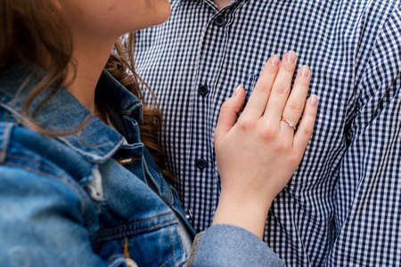 Hand of young woman with wedding ring on the chest of man in plaid shirt. Couple in love. Man and...