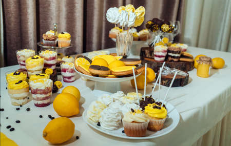 Holiday candy bar in yellow and brown color. Wedding candy bar served with cupcakes, cake pops, desserts in glasses, lemons and coffee beans の写真素材