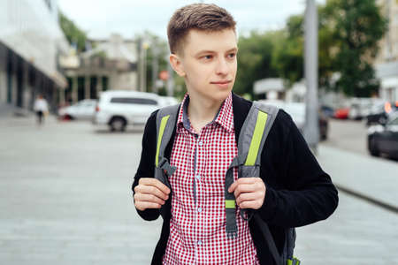 Portrait of stylish young man in plaid shirt and jacket with backpack walking in the city outdoors. Student travelの写真素材