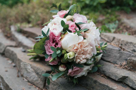Beautiful wedding bouquet of white and pink peony and roses in natural stone in blur outdoors, close upの写真素材