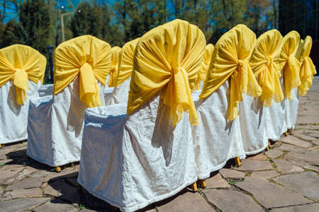 Chairs for guests on wedding ceremony with white and yellow satin cloth outdoorの写真素材