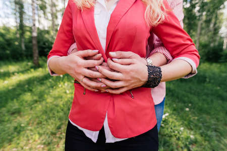 Hands of a couple in love. Man and woman are standing embracing and holding hands. Man hug woman in red jacketの写真素材
