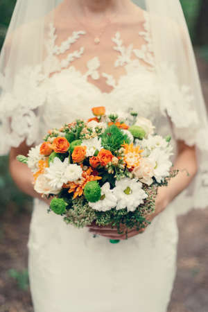 Wedding bouquet of orange roses, white and orange chrysanthemums and greenery in the bride's hands の写真素材
