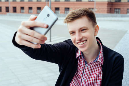 Stylish young smiling man in plaid shirt making selfie outdoors.Technology and communication concept...