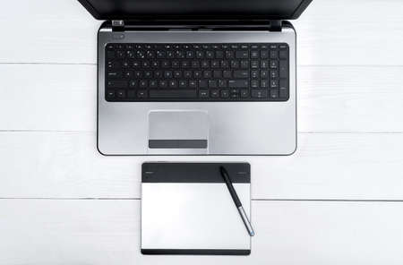 Wooden white office desk table with open blank laptop computer and graphic tablet, free space. Top view with copy space. Grey laptop with graphic tablet on wooden table backgroundの写真素材