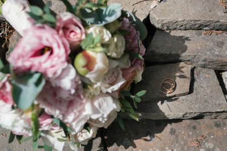 Two golden wedding rings on stone near   beautiful wedding bouquet of white and pink peony and roses in blur outdoors, close upの写真素材