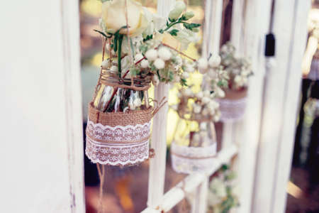 Little wedding floral decorations in rustic style hang in jars decorated with sacking and laceの写真素材