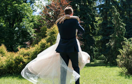 Young happy wedding couple dancing and having fun in sunny wedding day. Groom spinning bride. Dress develops in the wind. Groom holding happy emotional brideの写真素材