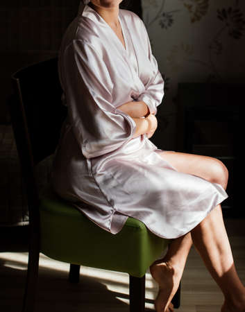 Beautiful young girl in silk robe sitting on chair and crosses her hands の写真素材