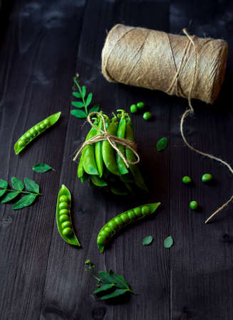 Bunch of fresh mature pods of green peas tied with a rope on black wooden background. Bio healthy food. Green peas, pods, pea leaves and twine on wooden tableの写真素材