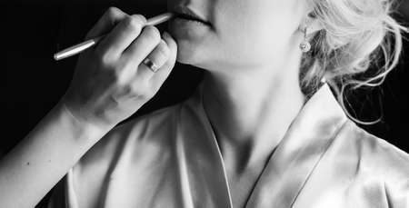 Closeup portrait of woman having applied makeup by makeup artist. Professional make-up artist applying lips makeup for girl in bathrobe. Makeup detail, black and white portraitの写真素材