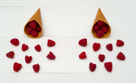 Sweet fresh organic raspberries in waffle cones. Fresh berries in cones on white wooden background...