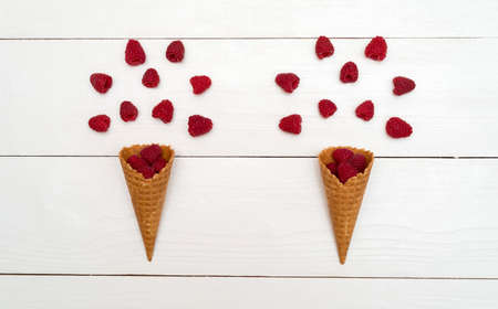 Top view of sweet fresh organic raspberries in waffle cones. Fresh berries in cones on white wooden background with blank space. Summer and healthy food concept flat layの写真素材
