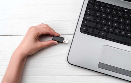 Hand inserting USB flash drive into laptop computer on white background. Close up of woman hand plugging pendrive on laptop at home. Copying data from flash drive to laptop computerの写真素材