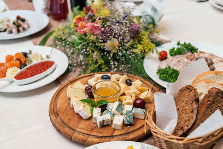 Cheese plate with cherries and honey on round wooden board plate on celebratory dinner table in blur, selective focus. Camembert, DorBlu, Emmental, Brie on cutting boardの写真素材