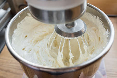 Closeup of electric mixer with whipped smooth dough for cake. Batter being whipped. Mixing white dough in bowl with motor mixer, baking cakeの写真素材