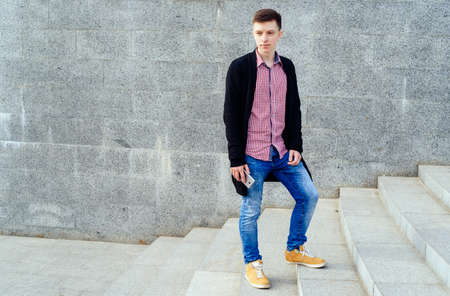 Stylish young man in plaid shirt and jeans walking up stairs and using smartphone outdoors. Student with smartphone walking up stairs, free spaceの写真素材
