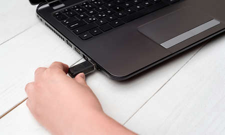 Hand inserting USB flash drive into laptop computer on white background. Close up of woman hand plugging pendrive on laptop at home. Copying data from flash drive to laptop computerの写真素材