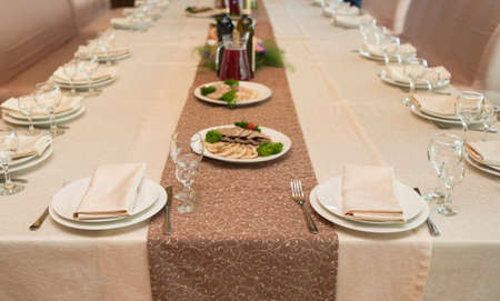 Beige serviette on white empty plate on dinner table in blur. Table setting in restaurant, selective focus. Table served for wedding banquet, close up view. の写真素材